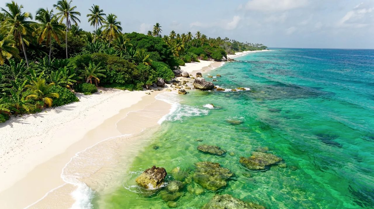 Vista aérea de uma praia caribenha em Curaçao, com águas cristalinas em tons de azul turquesa e verde, rodeada por exuberante vegetação tropical. Esta paisagem paradisíaca é um convite para férias inesquecíveis nas ilhas ABC.