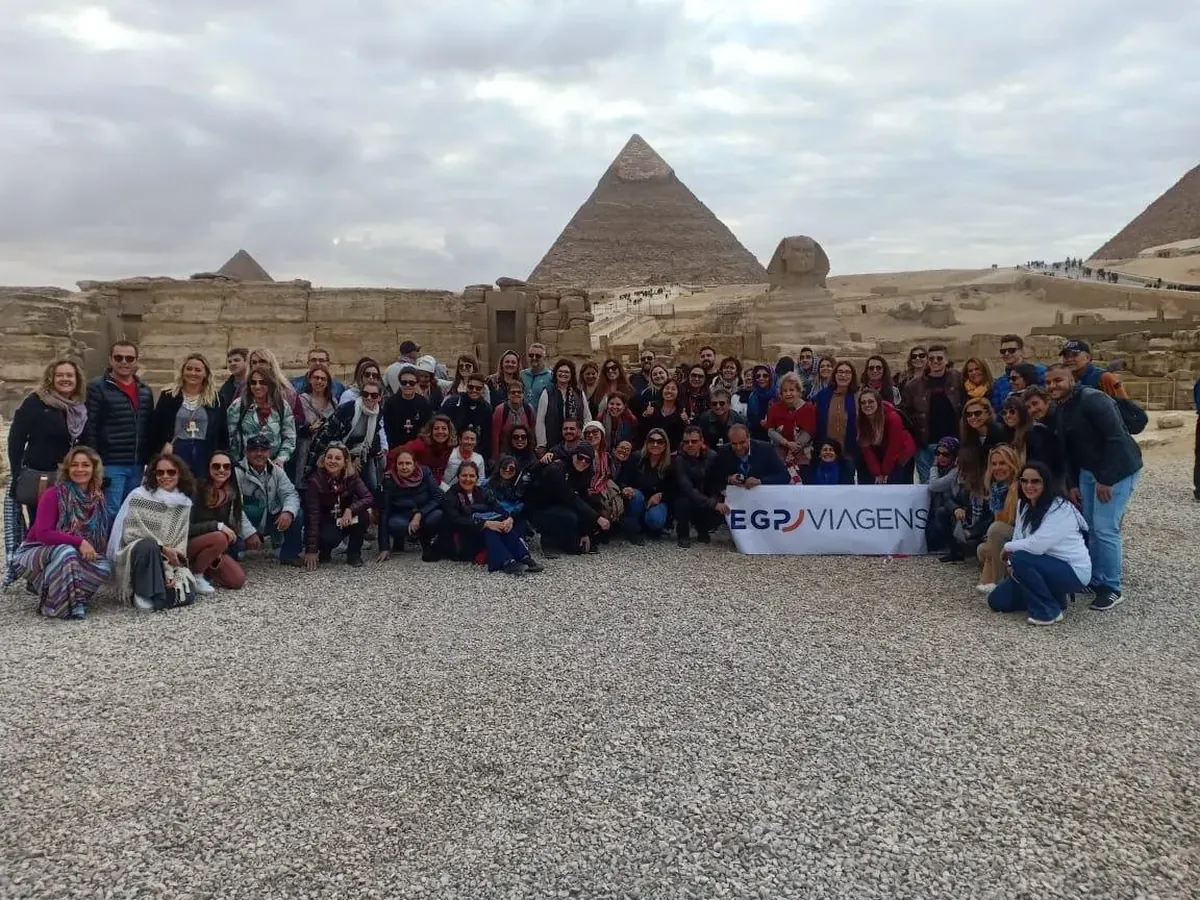 Grupo de clientes da EGP Viagens com a faixa da agência em frente à Esfinge e às Pirâmides de Gizé