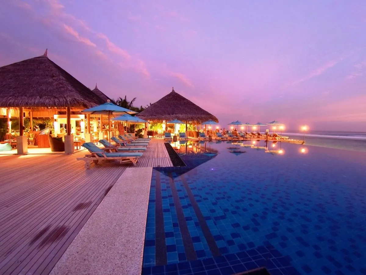 Um resort com piscina de borda infinita ao anoitecer, nas Maldivas