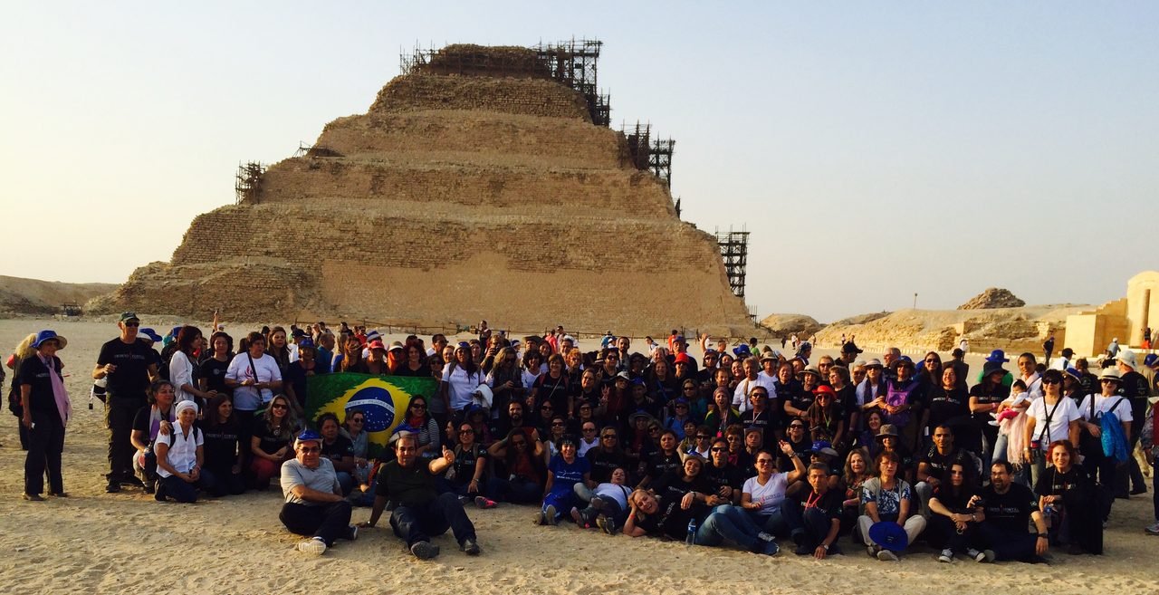 Grande grupo de clientes da EGP Viagens com bandeira do Brasil na Pirâmide de Degraus de Sacará, no Egito