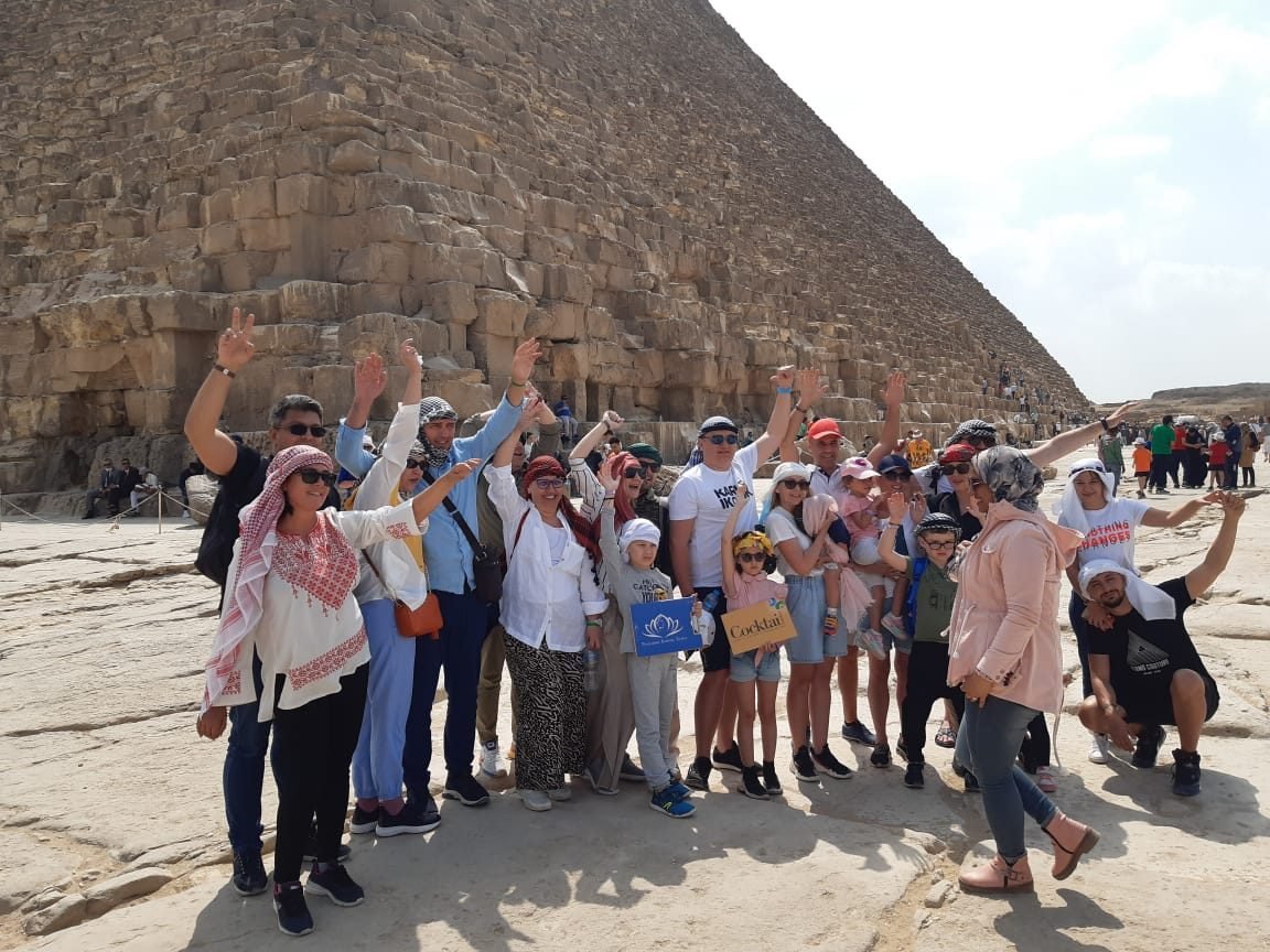 Grupo de clientes da EGP Viagens comemorando de mãos para o alto nas Pirâmides de Gizé, no Egito