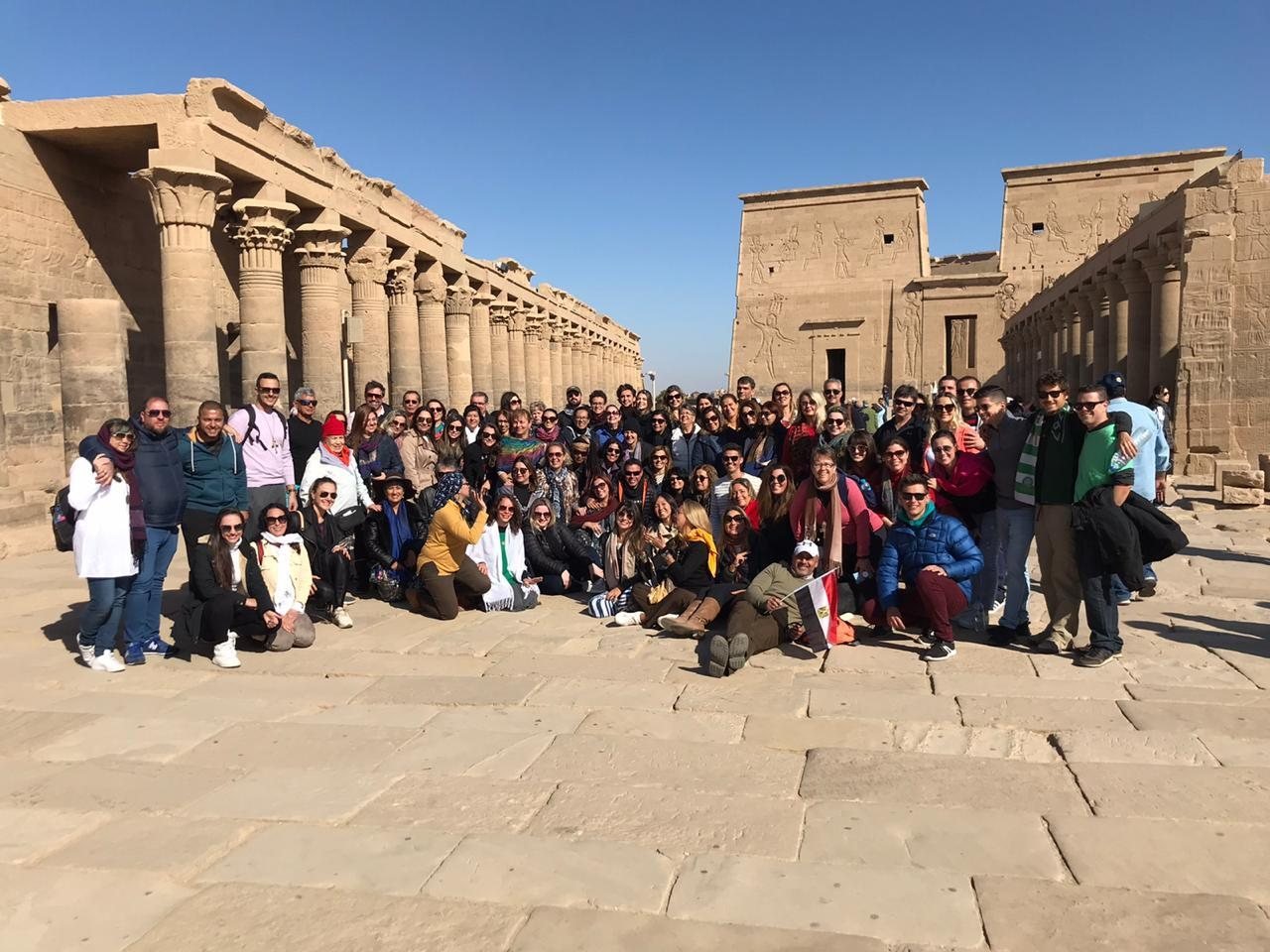 Grande grupo de clientes da EGP Viagens no Templo de Philae, em Aswan, Egito, segurando a bandeira do Egito