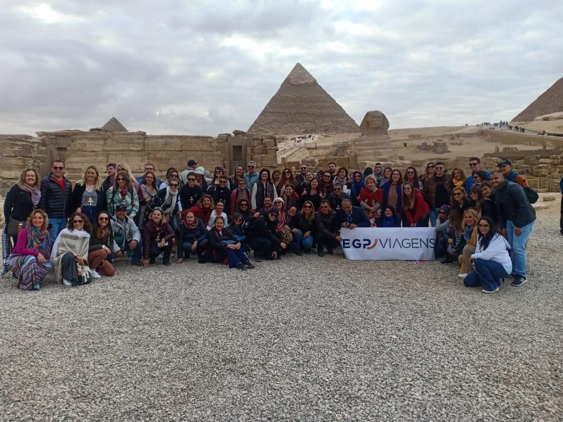 Grupo de clientes da EGP Viagens segurando faixa da EGP Viagens em frente à Esfinge e às Pirâmides de Gizé, no Egito