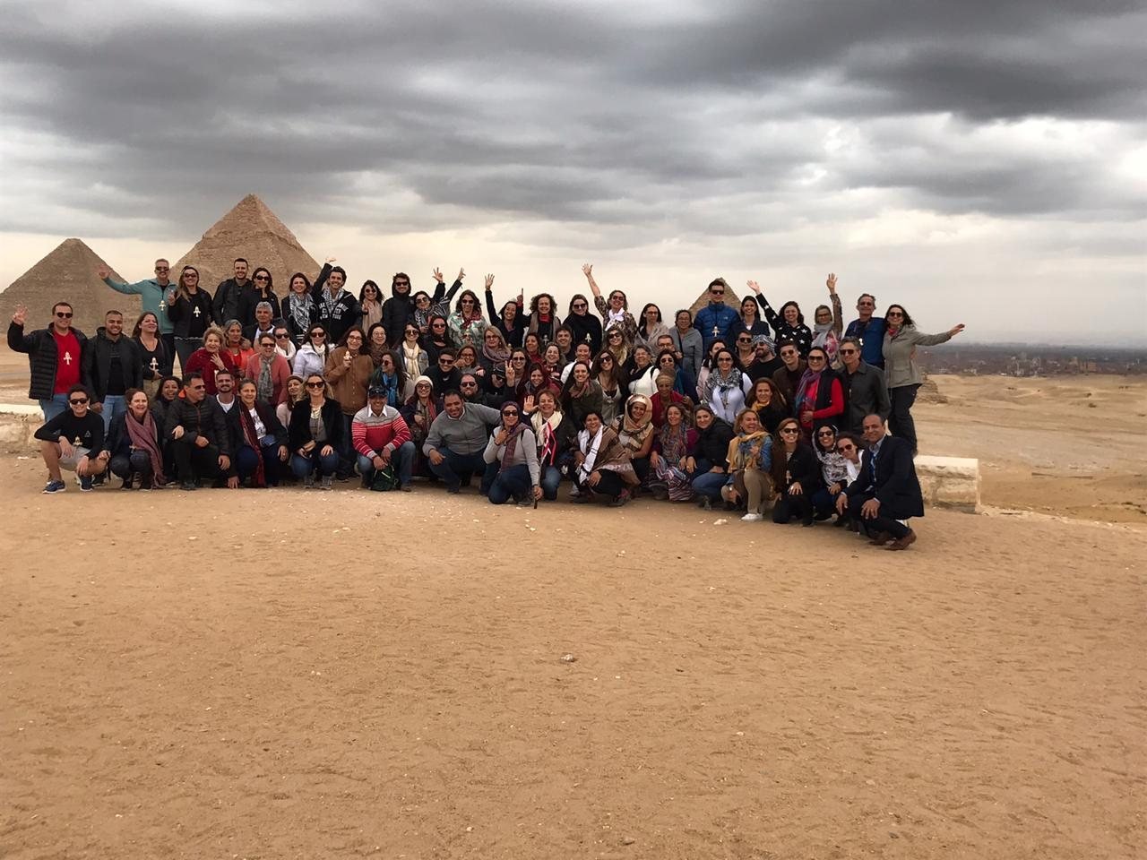 Grupo de clientes da EGP Viagens comemorando com as mãos para o alto em frente às Pirâmides de Gizé, no Egito