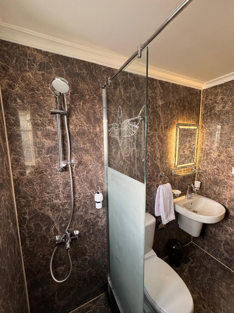 Banheiro com acabamento em mármore e detalhe egípcio gravado no vidro